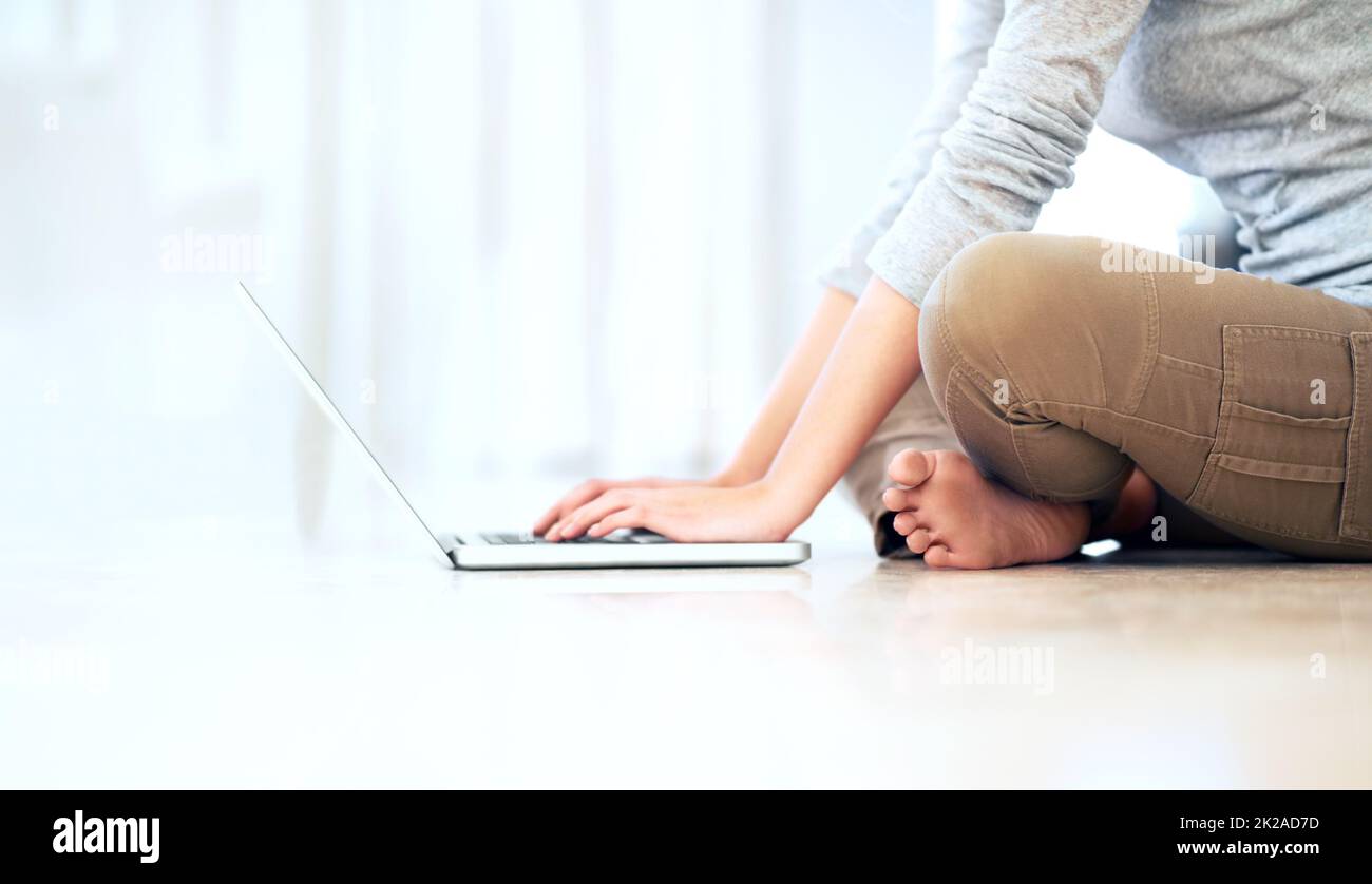 Von zu Hause aus – immer in Verbindung. Zugeschnittenes Bild einer jungen Frau, die auf dem Boden sitzt und ihren Laptop durchstöbert. Stockfoto
