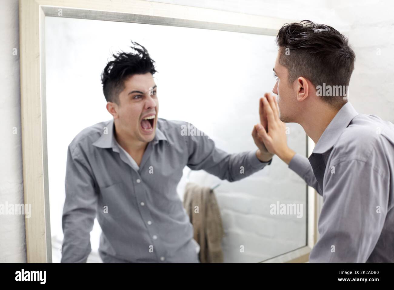 Unterdrückte Emotionen. Junger Mann, der in einem Spiegel eine schreiende Spiegelung seiner selbst ansieht. Stockfoto