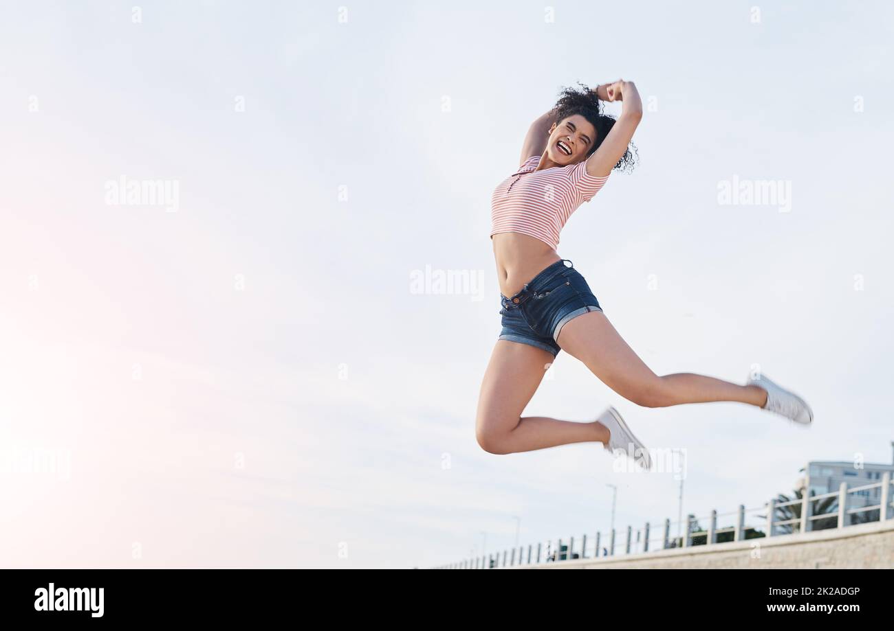 Raus und los geht es. Aufnahme einer jungen Frau, die am Strand in die Luft springt. Stockfoto