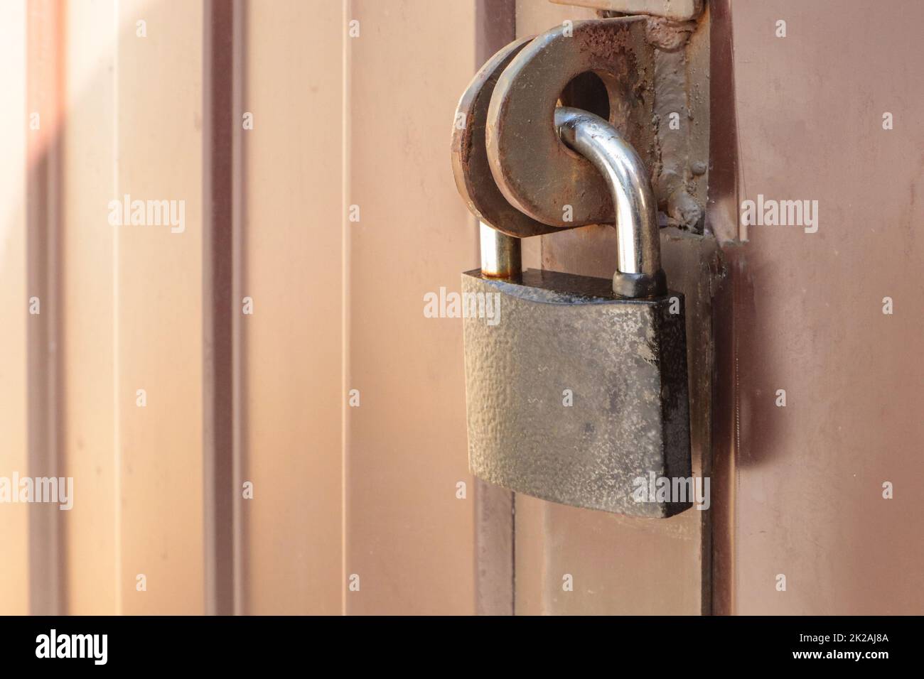 Ein Vorhängeschloss aus nächster Nähe am Tor eines braunen Metallzauns aus moderner Seitenverkleidung, dem Konzept der Sicherheit Stockfoto