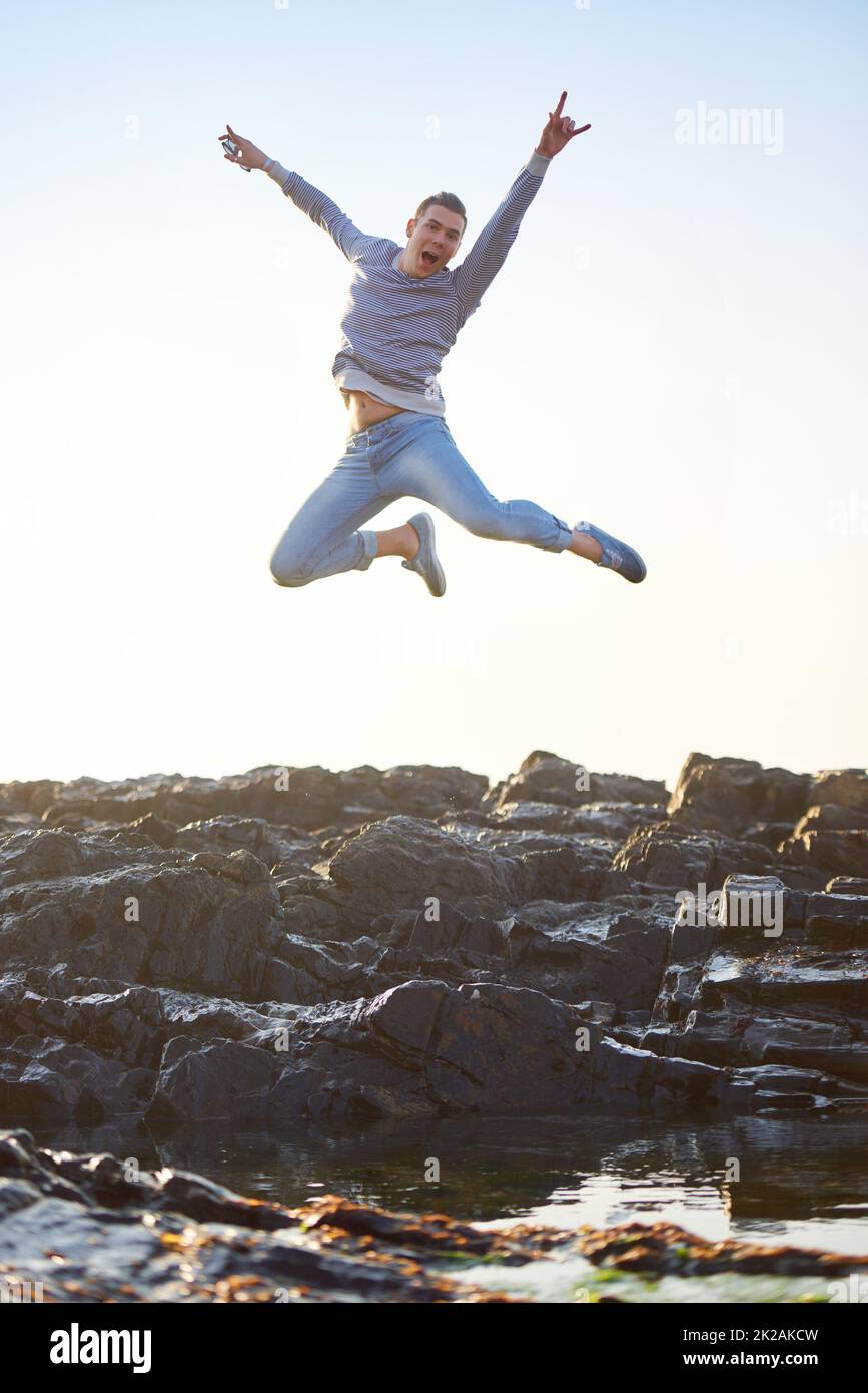 Die Energie freisetzen. Aufnahme eines hübschen jungen Mannes, der auf einem felsigen Strand springt. Stockfoto