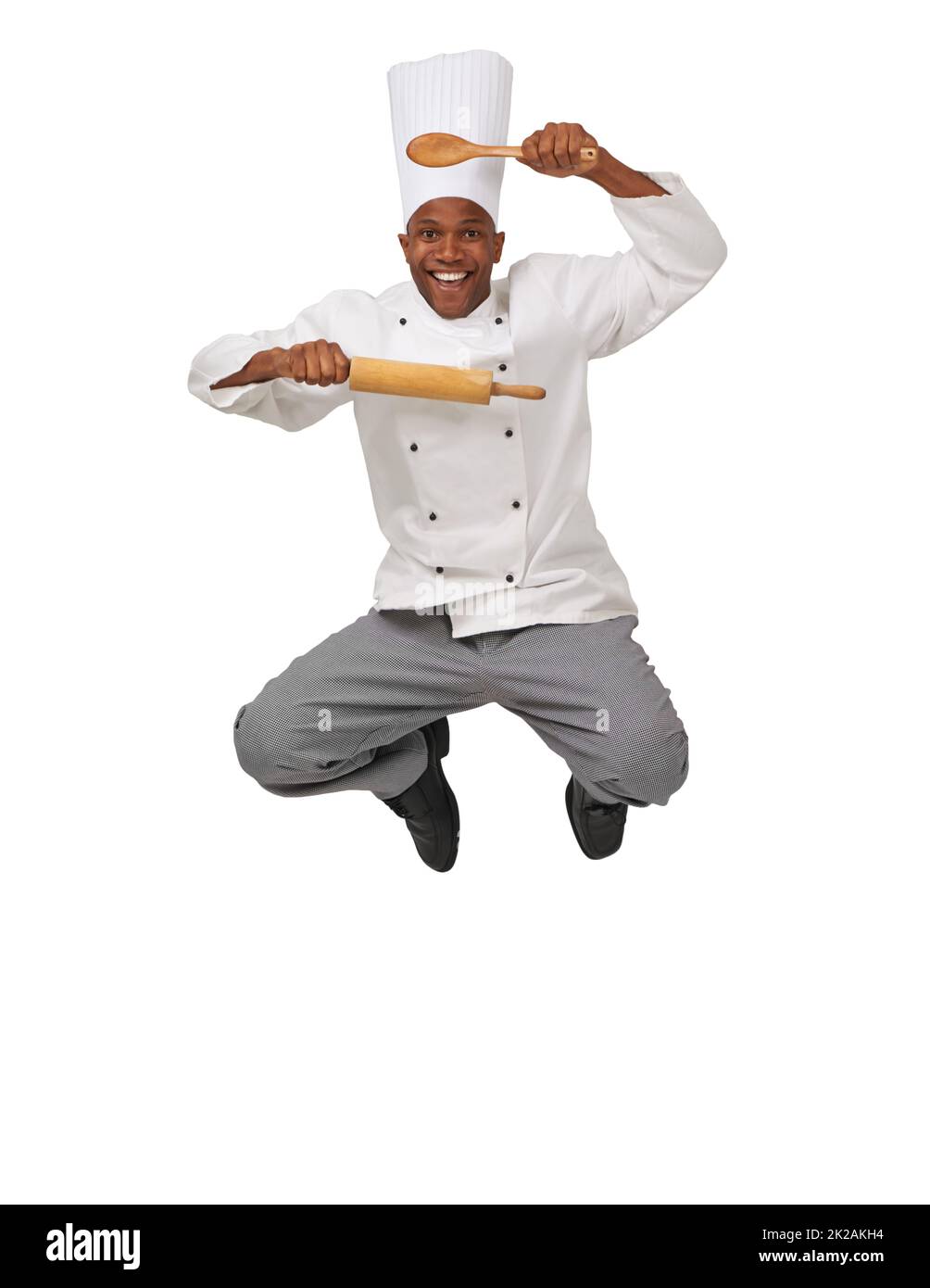 Köche Begeistern. EIN afroamerikanischer Koch springt in die Luft und hält eine Rolle und einen Löffel. Stockfoto