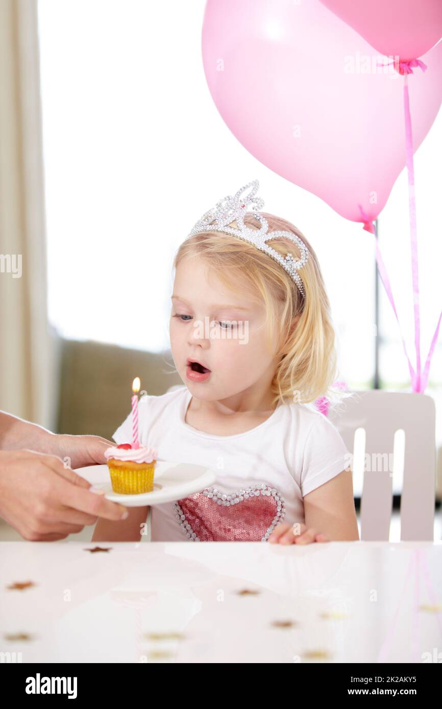 Ihr erster Geburtstag. Aufnahme eines niedlichen jungen Mädchens, das eine Kerze auf einem Cupcake ausbläst. Stockfoto