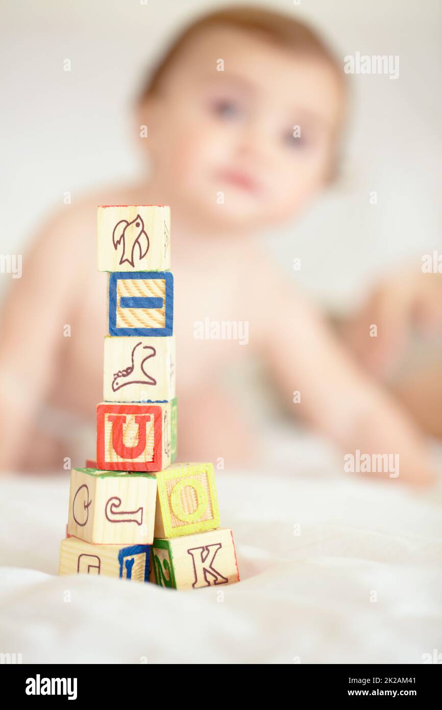 Bauen Sie heute auf die Zukunft Ihrer Kinder auf. Ein Turm aus Bausteinen im Vordergrund mit einem niedlichen Baby im Hintergrund. Stockfoto