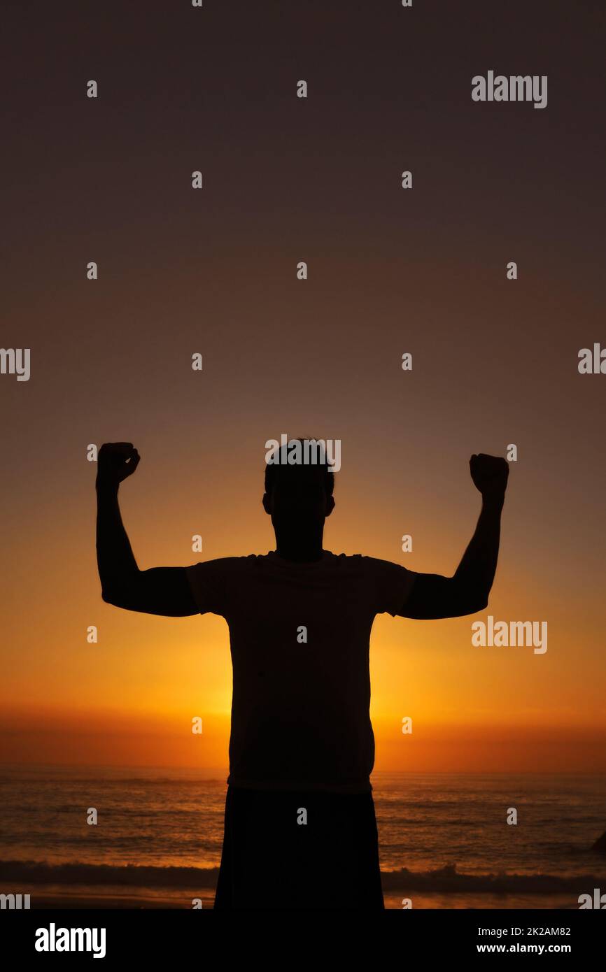Die Stromversorgung im Inneren finden. Silhouette eines Mannes, der mit seinen Armen gegen den Sonnenuntergang siegreich angehoben steht. Stockfoto