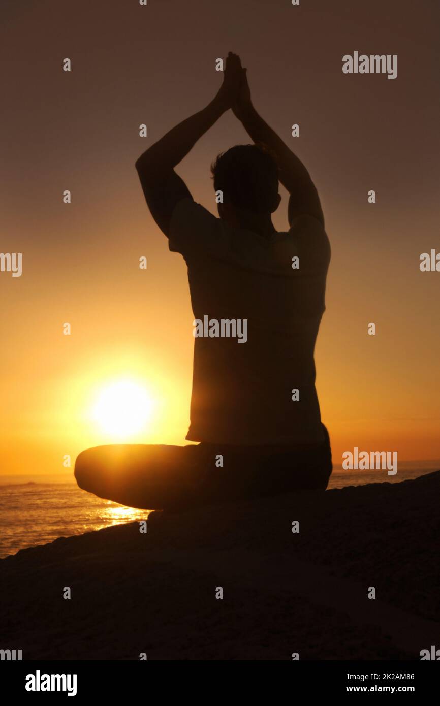 Sich mit dem Universum eins fühlen. Silhouette eines Mannes gegen den Sonnenuntergang mit erhobenen Armen in Yoga-Pose. Stockfoto