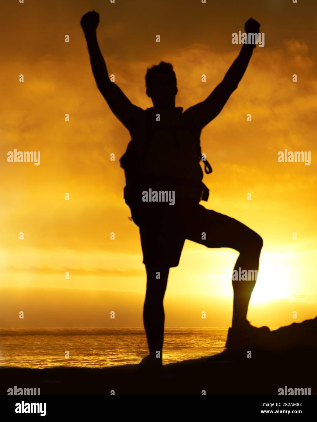 Den Berg erobern. Silhouette eines Wanderers, der mit erhobenen Armen auf einem Berg steht. Stockfoto