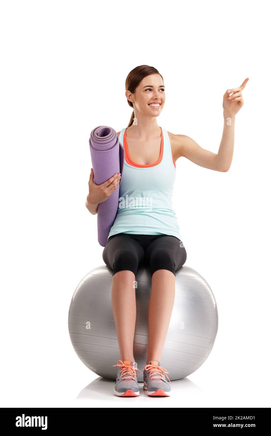 Finden Sie Ihre Motivation und verlieren Sie sie nicht. Aufnahme einer jungen Frau, die mit ihrer Yogamatte und ihrem Gymnastikball auf etwas in einem Studio zeigt. Stockfoto