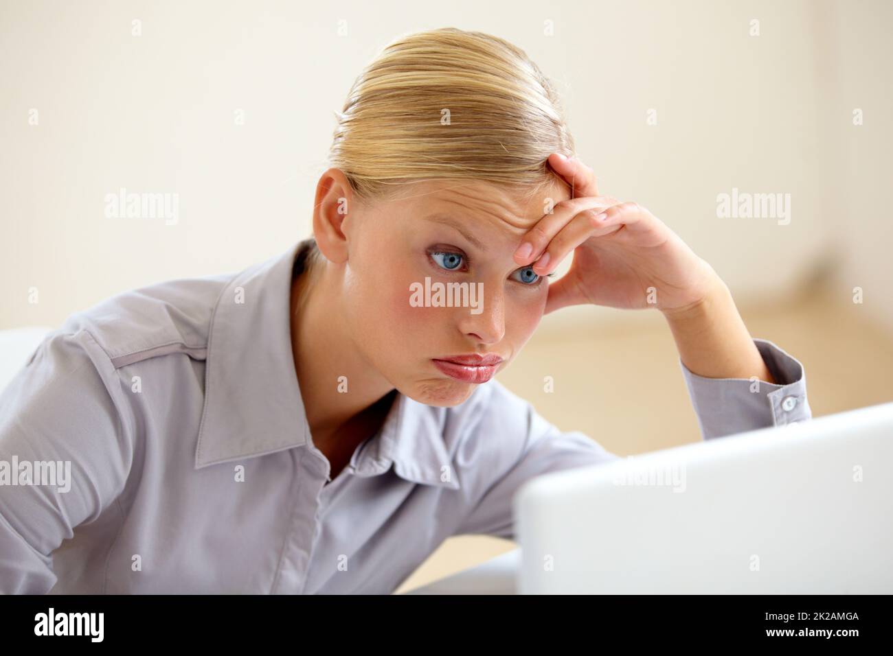 Es gibt noch mehr zu tun. Eine erschöpfte junge Frau, die ihren Laptop-Bildschirm mit einem Stirnrunzeln ansieht. Stockfoto