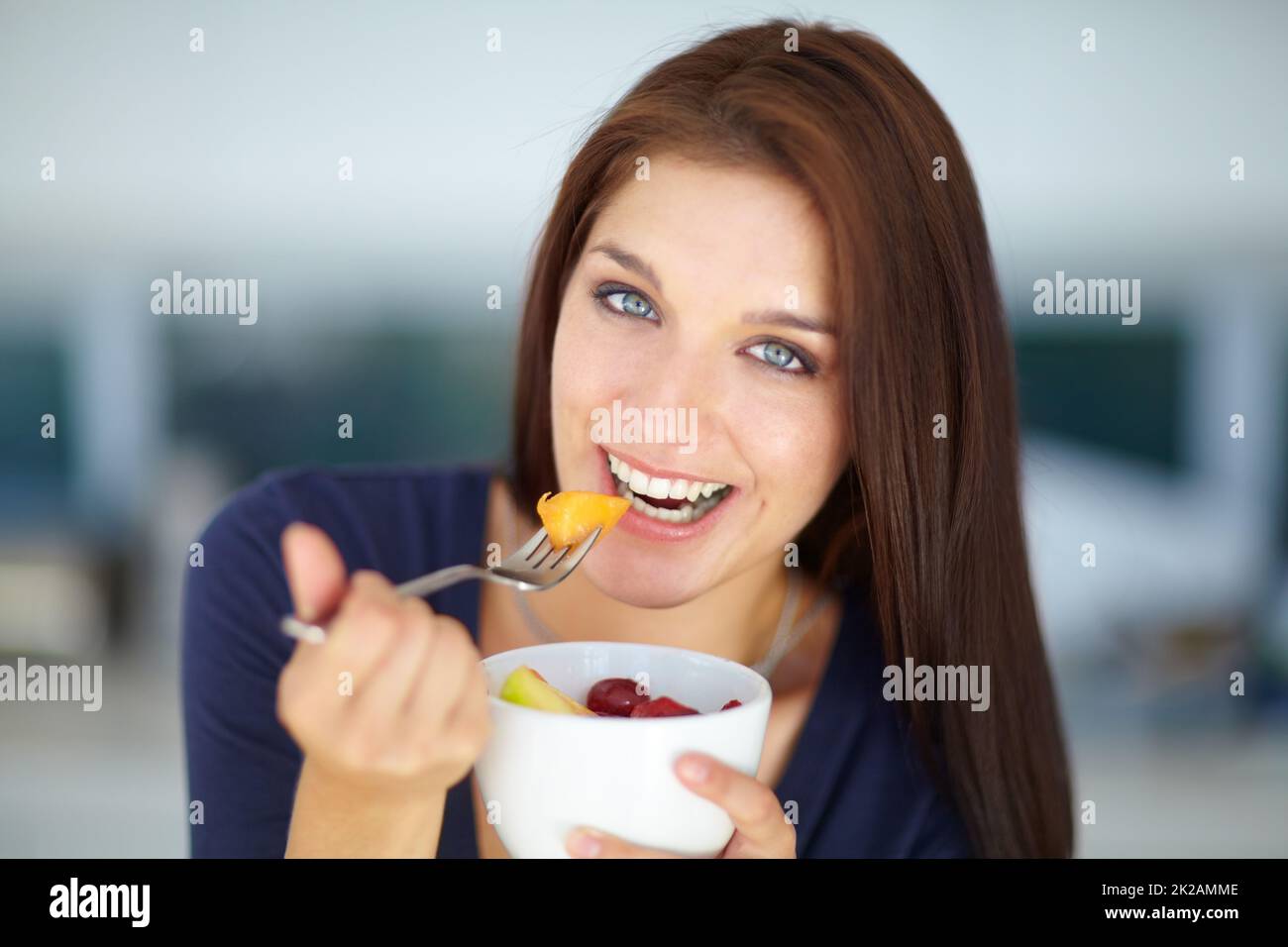 Genießen Sie einen leckeren, gesunden Snack. Porträt einer lächelnden jungen Frau, die mittags einen gesunden Obstsalat isst. Stockfoto