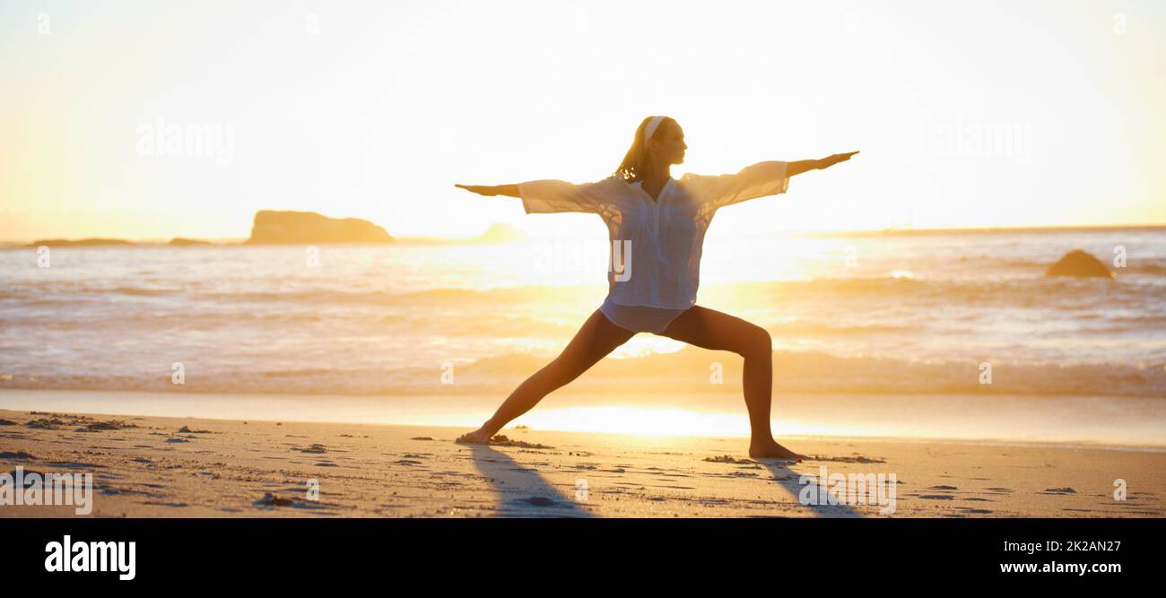 Ruhig und friedlich. Ruhige Szene einer jungen Frau, die am Strand bei Sonnenuntergang eine Pilates-Pose macht. Stockfoto