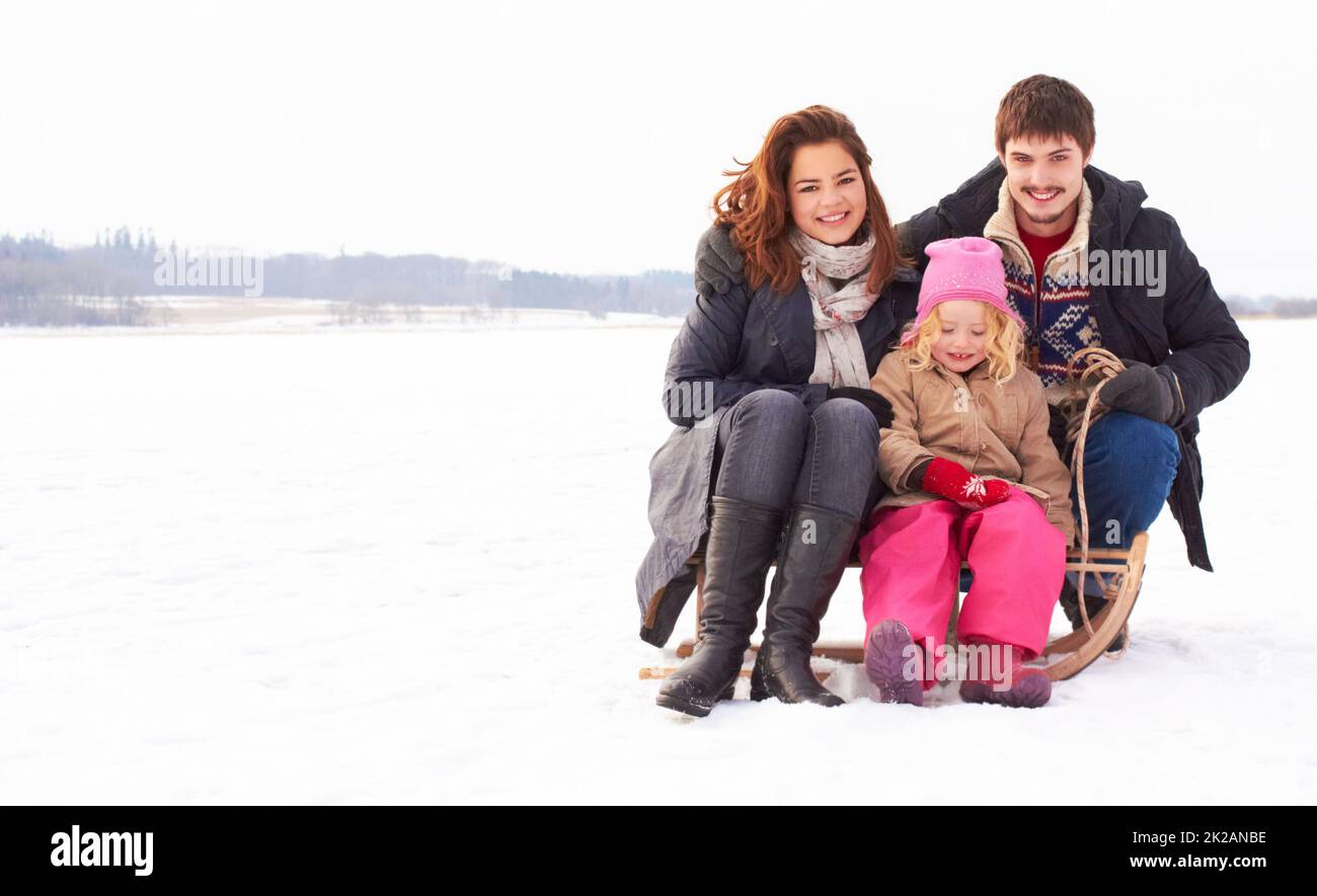 Bindungszeit auf dem Eis. Zwei Jugendliche und ein Kind, die an einem frischen Wintertag auf einem Schneelitten im Freien sitzen. Stockfoto
