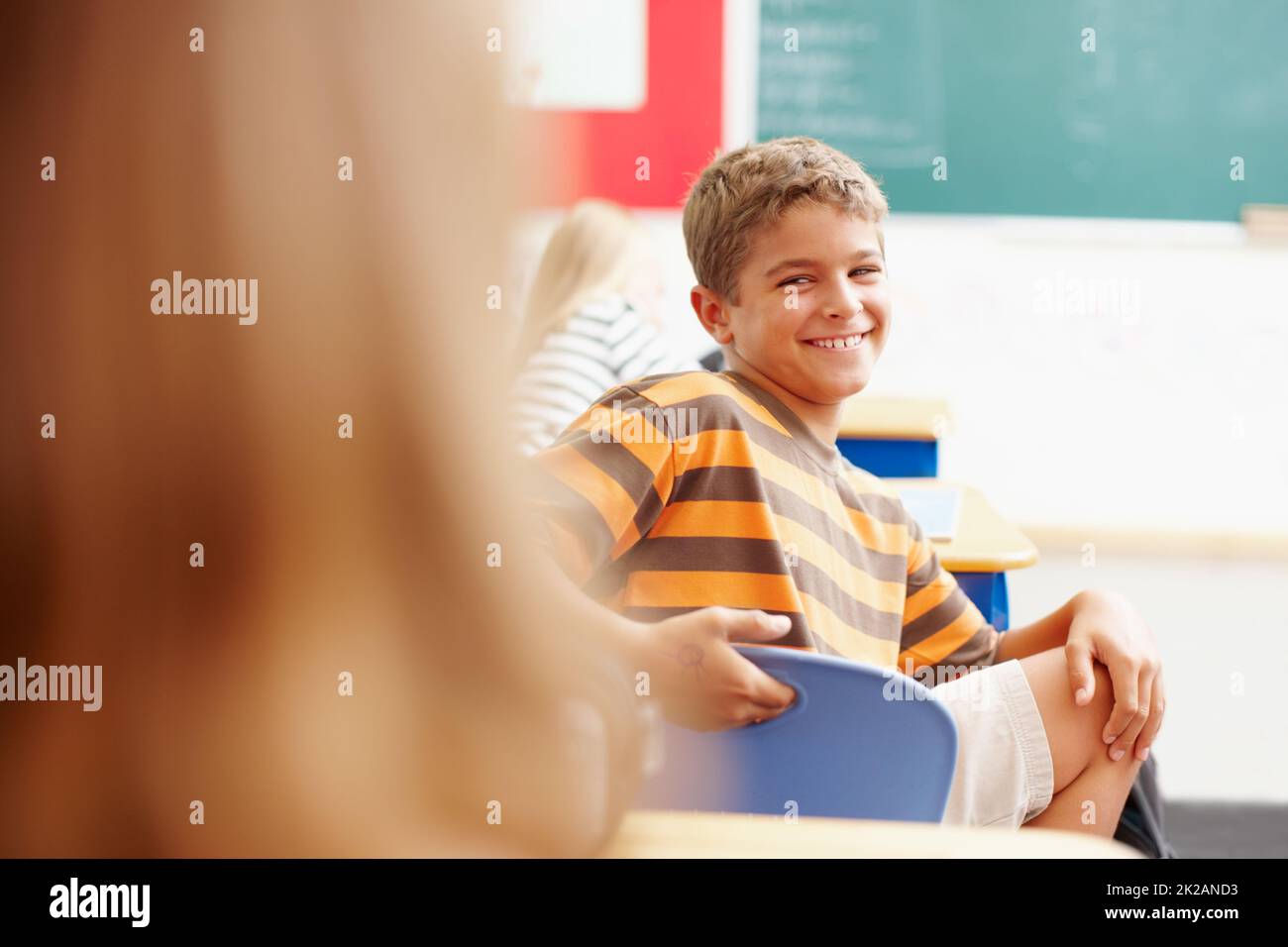 Holen Sie sich die Aufmerksamkeit des coolen Kindes in der Klasse. Lächelnder Junge dreht sich in der Klasse um, um einen Klassenkameraden zu betrachten - Copyspace. Stockfoto