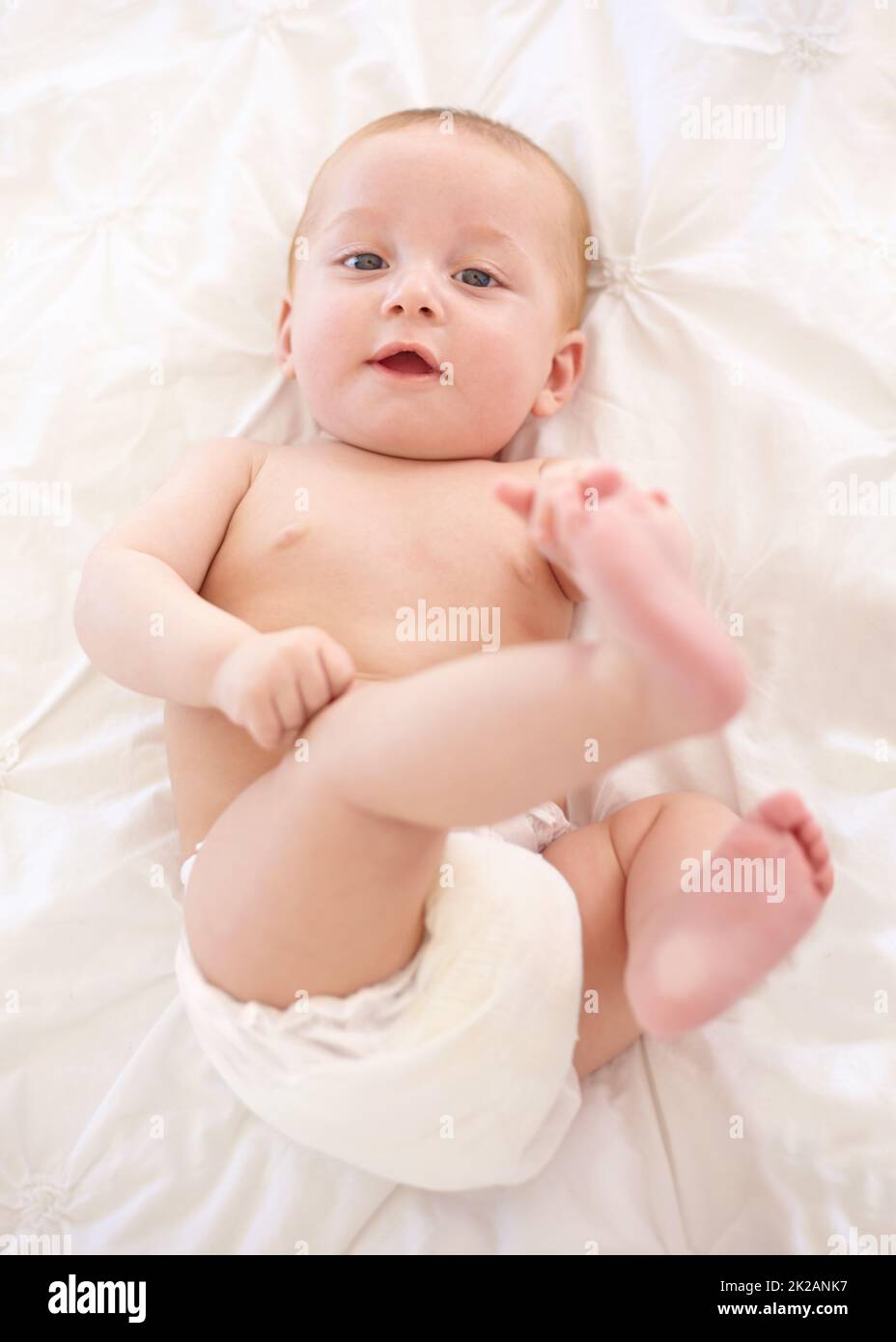 Es gibt eine große weite Welt zu erkunden.... Niedliches kleines Baby, das sich hinlegt und seine Füße berührt. Stockfoto