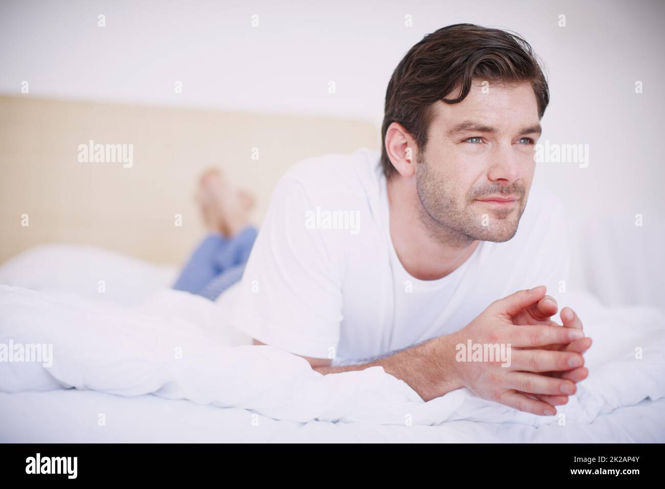 Denken wir über einige Dinge nach Ein hübscher junger Mann, der auf seinem Bauch auf einem Bett liegt und nachdenklich aussieht. Stockfoto