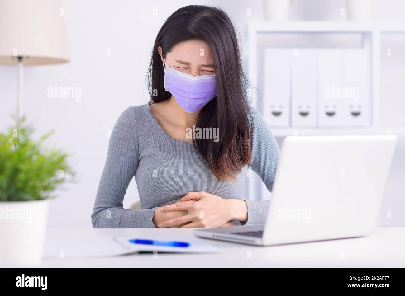 Junge Frau mit Bauchschmerzen im Büro Stockfoto