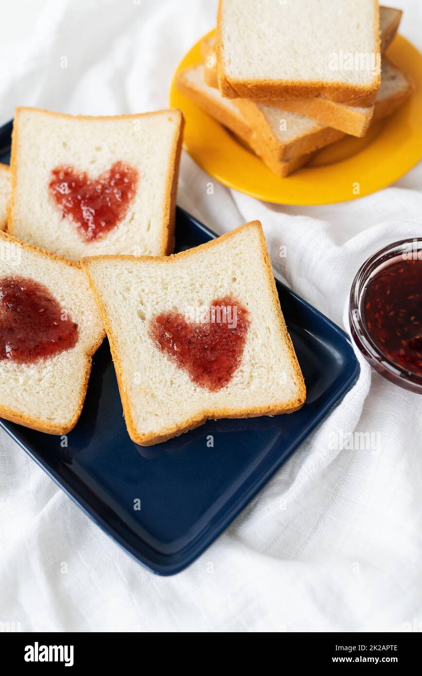 Toast, auf dem das Herz aus Marmelade besteht. Überraschendes Frühstückskonzept im Bett. Romantik für St. Valentinstag. Stockfoto