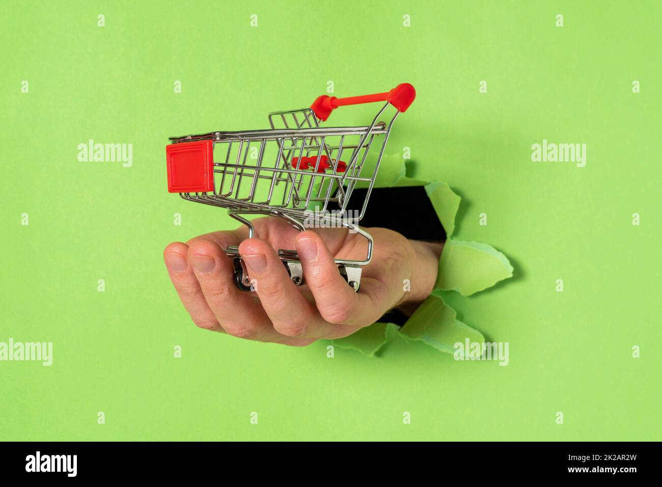 Die Hand mit dem Einkaufswagen ragt aus einem zerrissenen Loch im Papier heraus Stockfoto