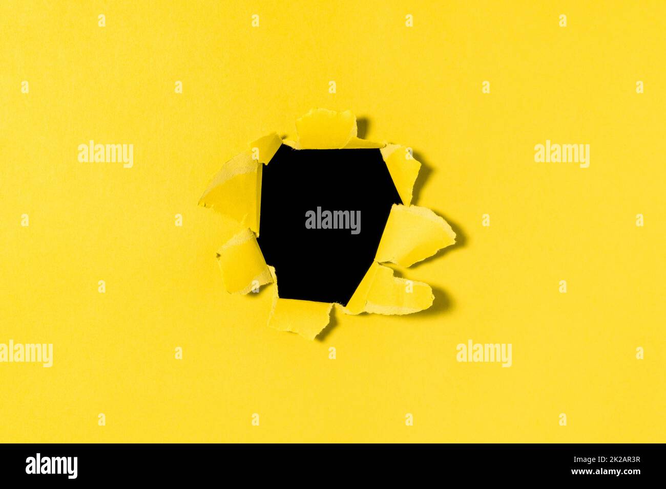 Ein Loch in gelbem Papier mit gerissenen Kanten und schwarzem Hintergrund im Inneren Stockfoto