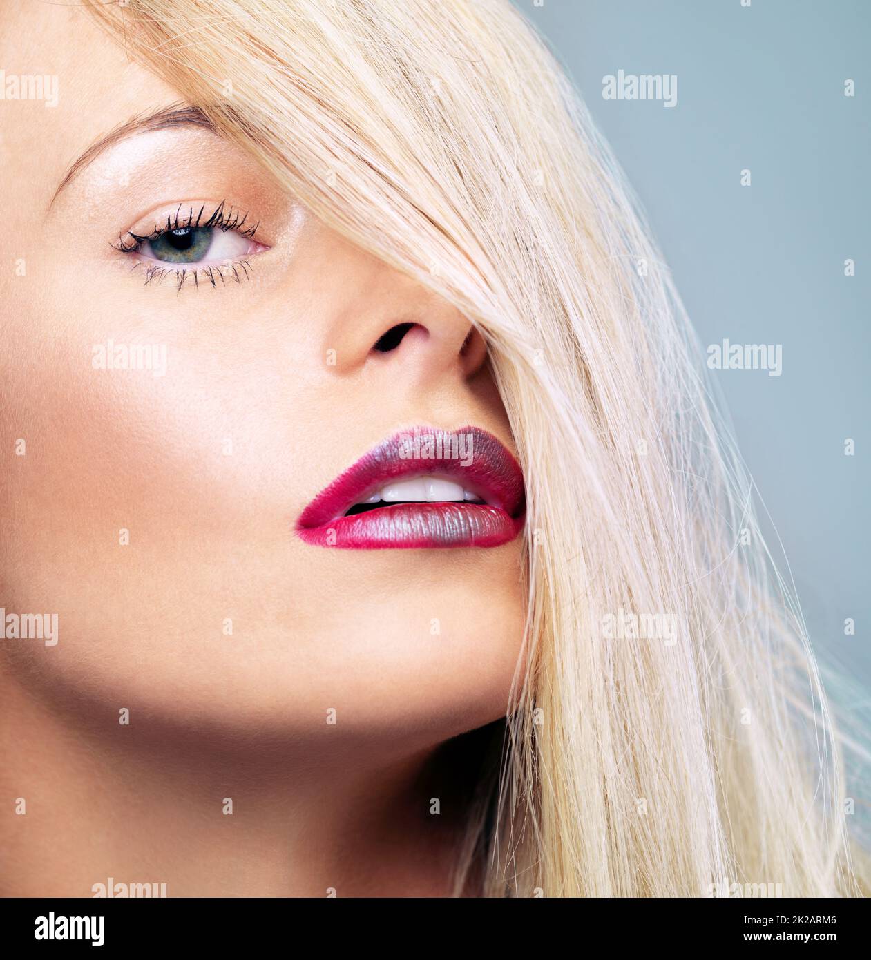 Leuchtend rote Schönheit. Nahaufnahme einer jungen blonden Frau mit einem leuchtend roten Lippenstift vor grauem Hintergrund. Stockfoto