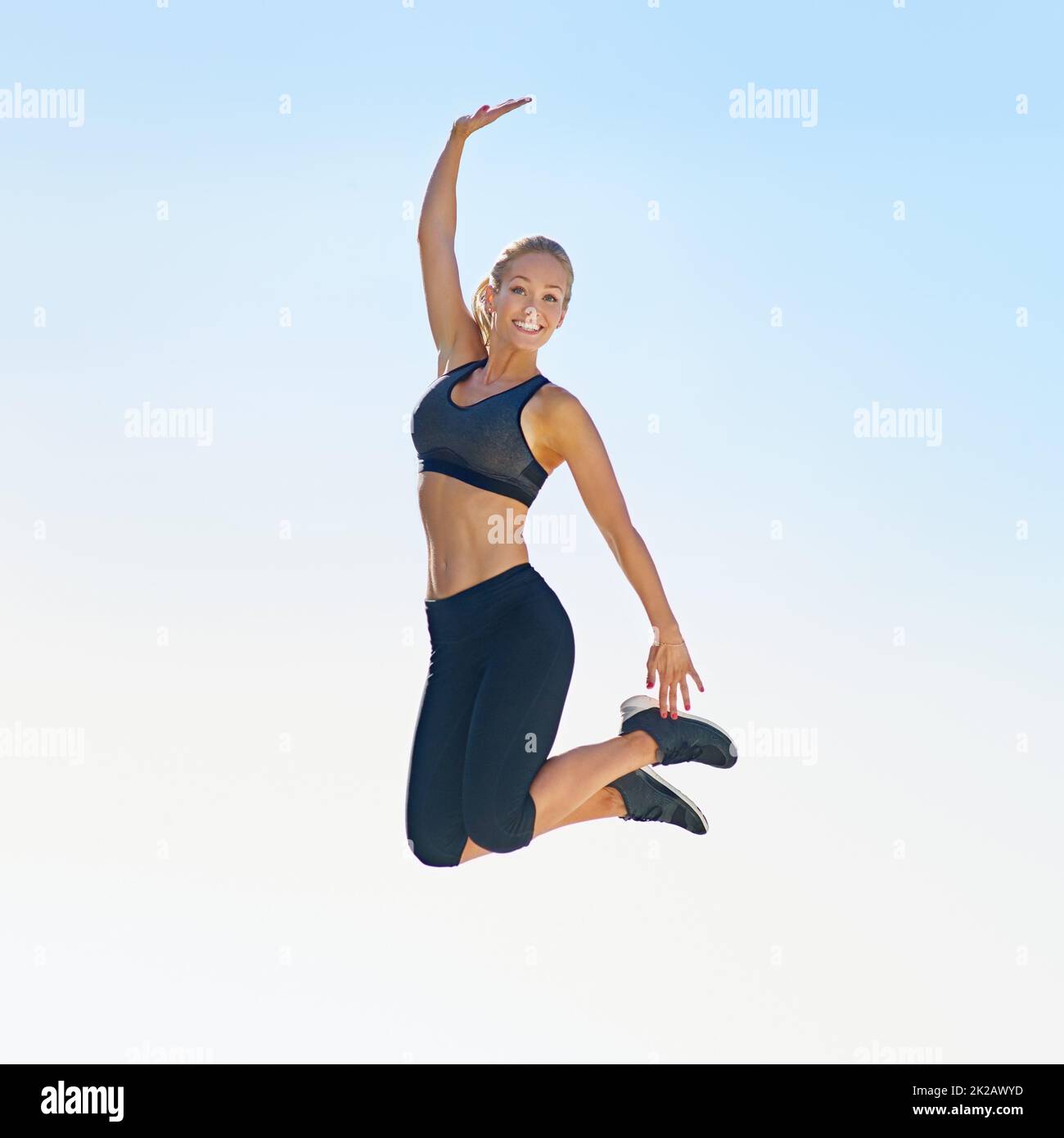 Es fühlt sich gut an, fit zu sein. Ganzkörperaufnahme einer sportlichen jungen Frau, die gegen einen blauen Himmel springt. Stockfoto