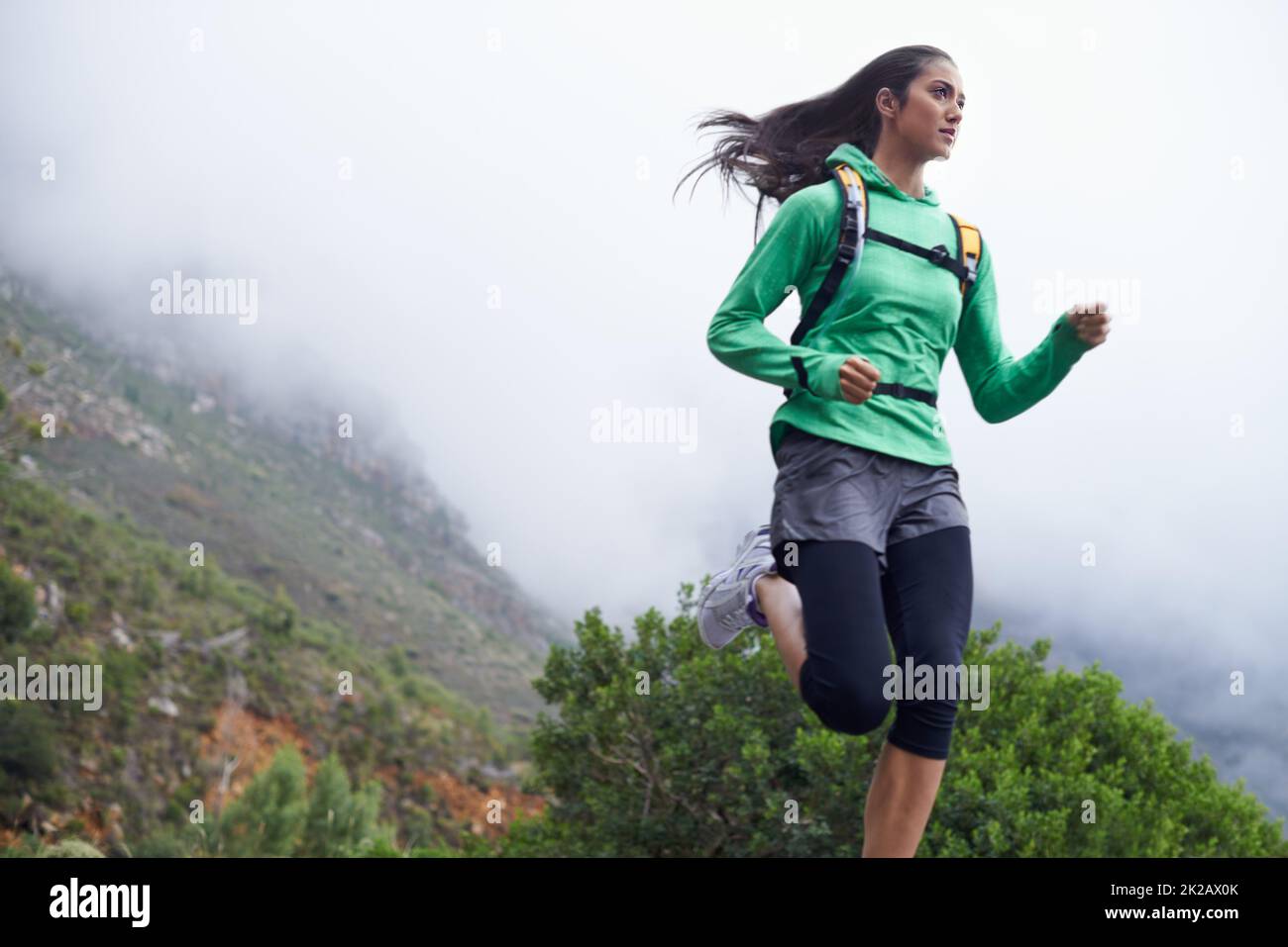Sie schreitet jeden Tag in ihrer Fitness voran. Eine junge Frau sprintet an einem frischen Morgen entlang einer Bergstraße. Stockfoto