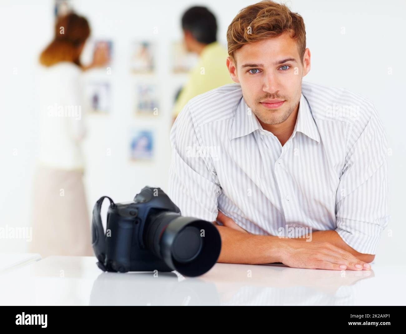 Fotograf sitzt am Tisch. Porträt eines Fotografen, der am Tisch sitzt, und Menschen, die sich Bilder im Hintergrund ansehen. Stockfoto