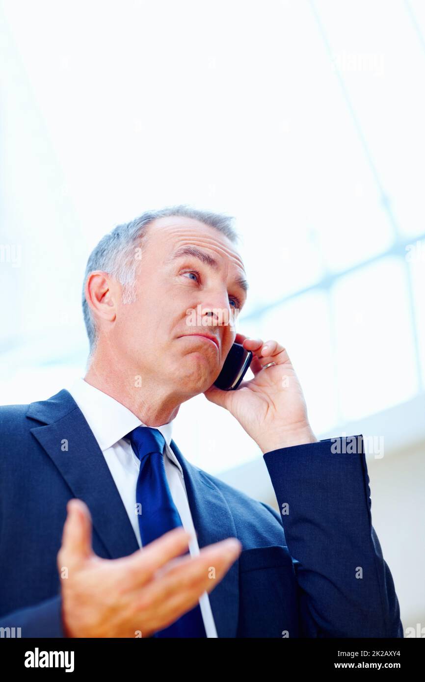 Der Manager sieht beim Telefonieren unsicher aus. Leitender Angestellter mit verwirrtem Blick, während er auf dem Handy ist. Stockfoto