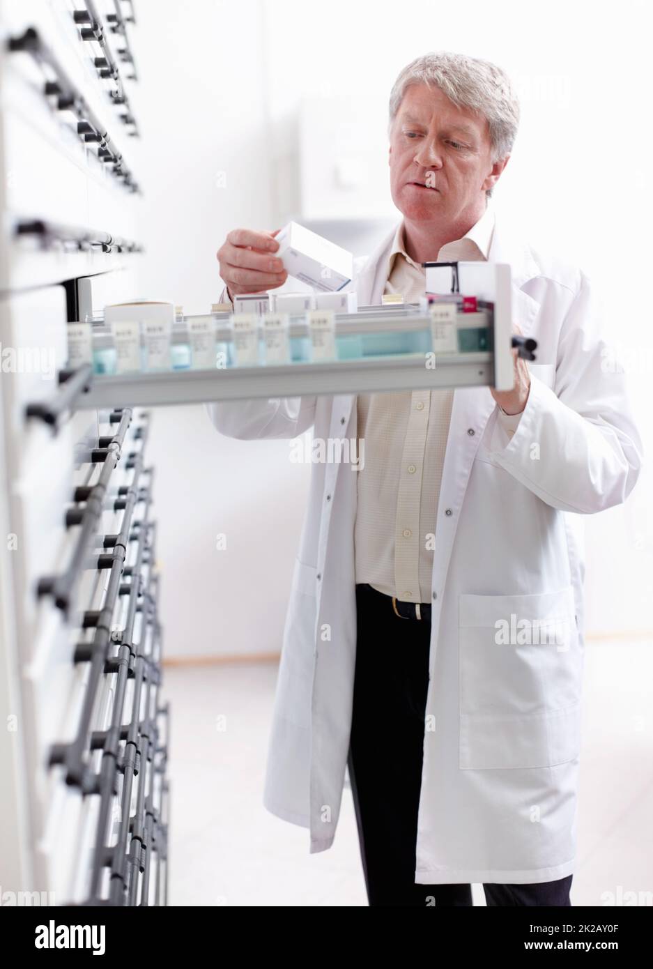 Apotheker auf der Suche nach Medikamenten im Regal. Porträt eines reifen Apothekers, der in der Apotheke im Regal nach Medikamenten sucht. Stockfoto