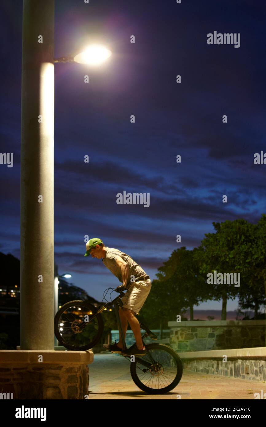 Schlafen Sie nie - fahren Sie einfach. Aufnahme eines Mannes, der nachts unter einer Straßenbeleuchtung Tricks auf seinem Fahrrad macht. Stockfoto