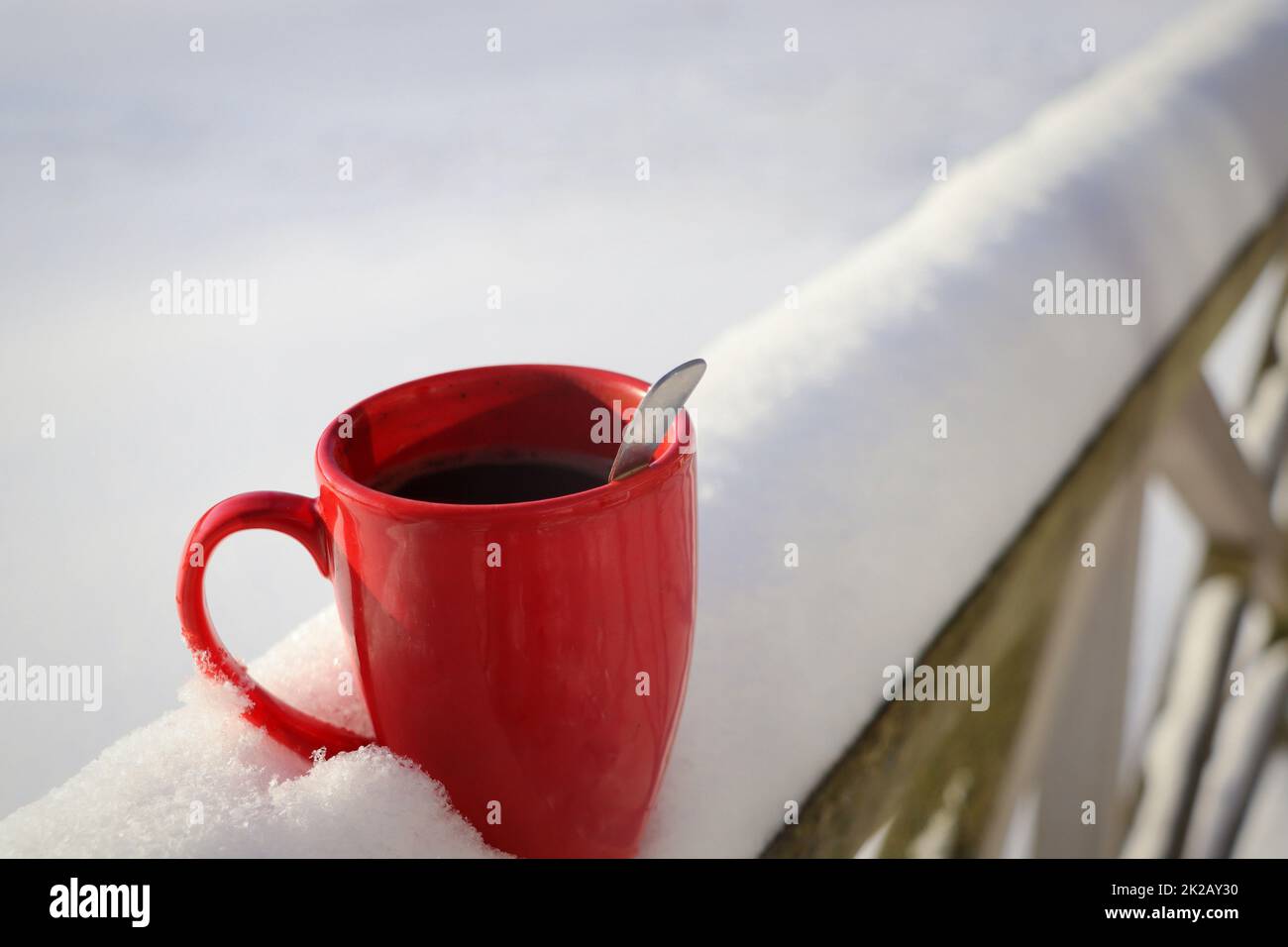 Dampfende Tasse heißen Kaffees oder Tees stehen am verschneiten Wintermorgen auf dem Tisch im Freien. Gemütlicher festlicher roter Becher mit einem warmen Getränk im Wintergarten. Das Weihnachtsmorgenkonzept Stockfoto