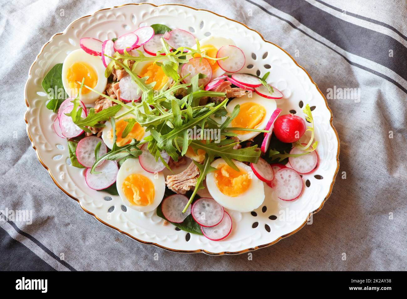 Frischer Salat mit Thunfisch, Rettich, Eiern, Rucola d auf grauem Hintergrund, Draufsicht. Gesunde Ernährung. Frühlingssalat Stockfoto