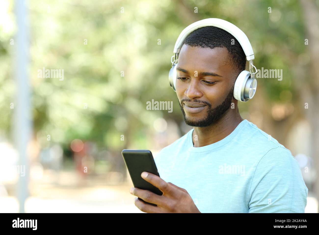 Ein Mann mit schwarzer Haut, der Musik hört, während das Telefon im Park ist Stockfoto
