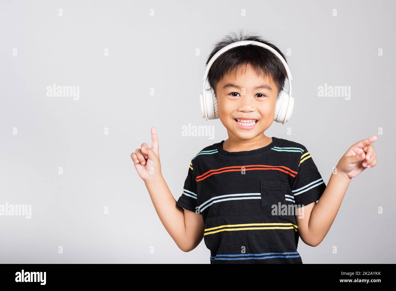 Kleiner süßer Junge 5-6 Jahre Hören Sie Musik in kabellosen Kopfhörern im Studio isoliert. Kleiner süßer Junge 5-6 Jahre Hören Sie Musik in kabellosen Kopfhörern im Studio isoliert auf weißem Hintergrund, glückliche asiatische Kinder lächeln und hören Audio A Stockfoto
