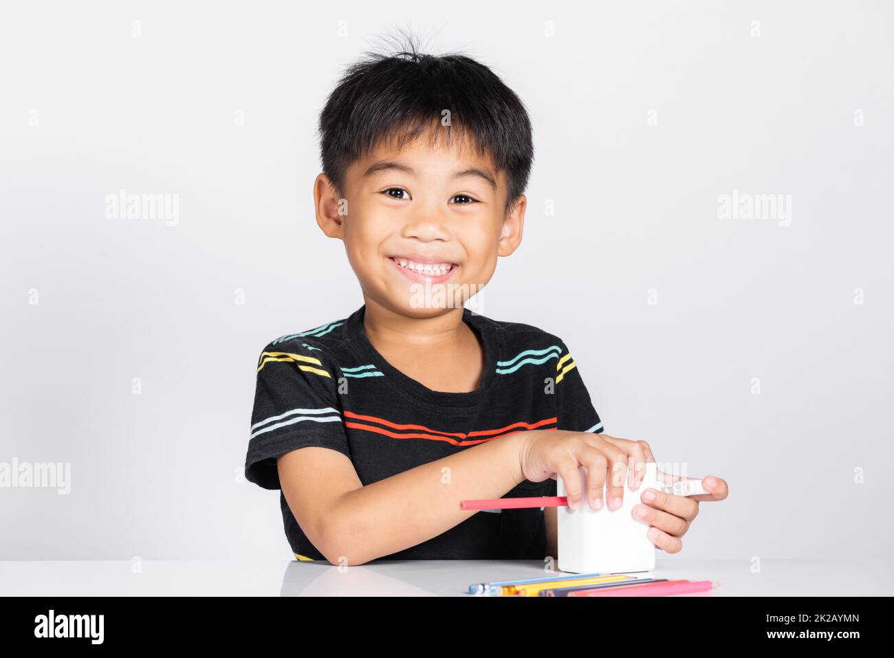 Der kleine süße Junge im Alter von 5-6 Jahren lächelt mit einem Bleistiftspitzer, während er Hausaufgaben macht Stockfoto