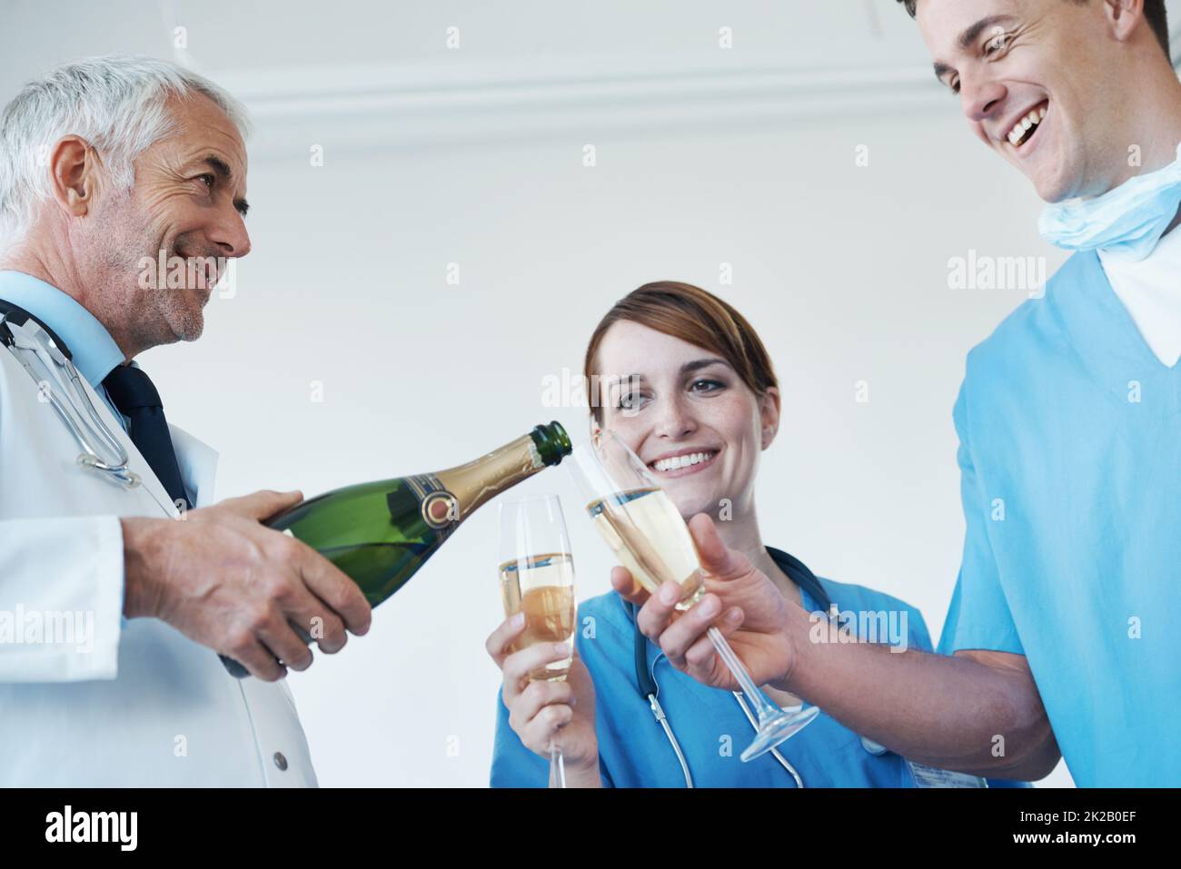 Jubel zu einem erfolgreichen Eingriff. Ein Hausarzt, eine Krankenschwester und ein Chirurg trinken zusammen Champagner nach einem erfolgreichen Eingriff. Stockfoto