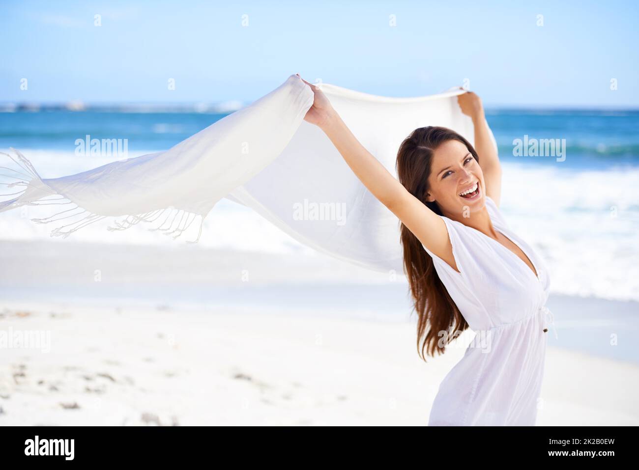 Loslassen und sich im Freien Vergnügen. Eine wunderschöne junge Frau am Strand, die einen weißen Schal hält, der im Wind weht. Stockfoto