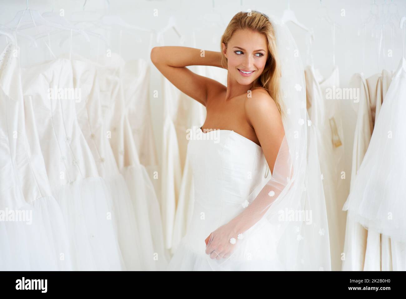 Den perfekten Schleier aussuchen. Eine junge Braut, die ihr Hochzeitskleid anprobiert - Copyspace. Stockfoto
