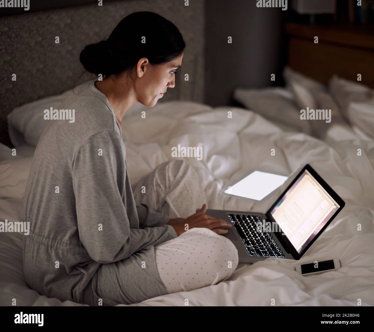 Erledigen Sie einige Aufgaben bequem von zu Hause aus. Eine junge Frau, die im Bett an ihrem Laptop arbeitet. Stockfoto