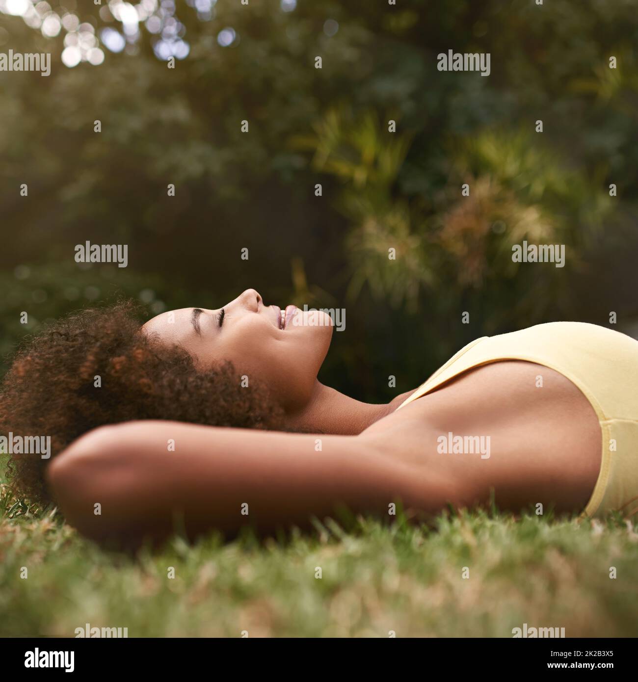 Entspannen an einem goldenen Nachmittag ... Aufnahme einer entspannten jungen Frau, die mit geschlossenen Augen auf dem Gras liegt. Stockfoto