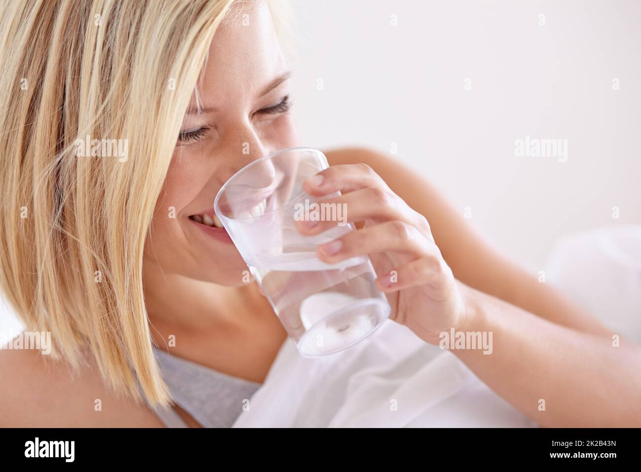 Sie trinkt immer ein Glas Wasser vor dem Bett. Eine junge Frau, die vor dem Bett ein Glas Wasser trinkt. Stockfoto