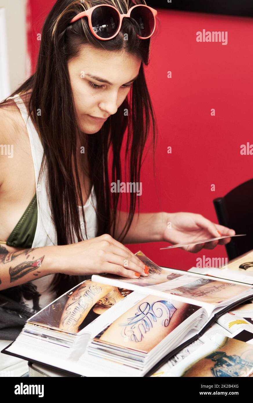 Das richtige Design für ihre Kollektion zu finden. Aufnahme einer schönen jungen tätowierten Frau, die durch ein Album mit Tattoo-Designs blättern soll. Stockfoto