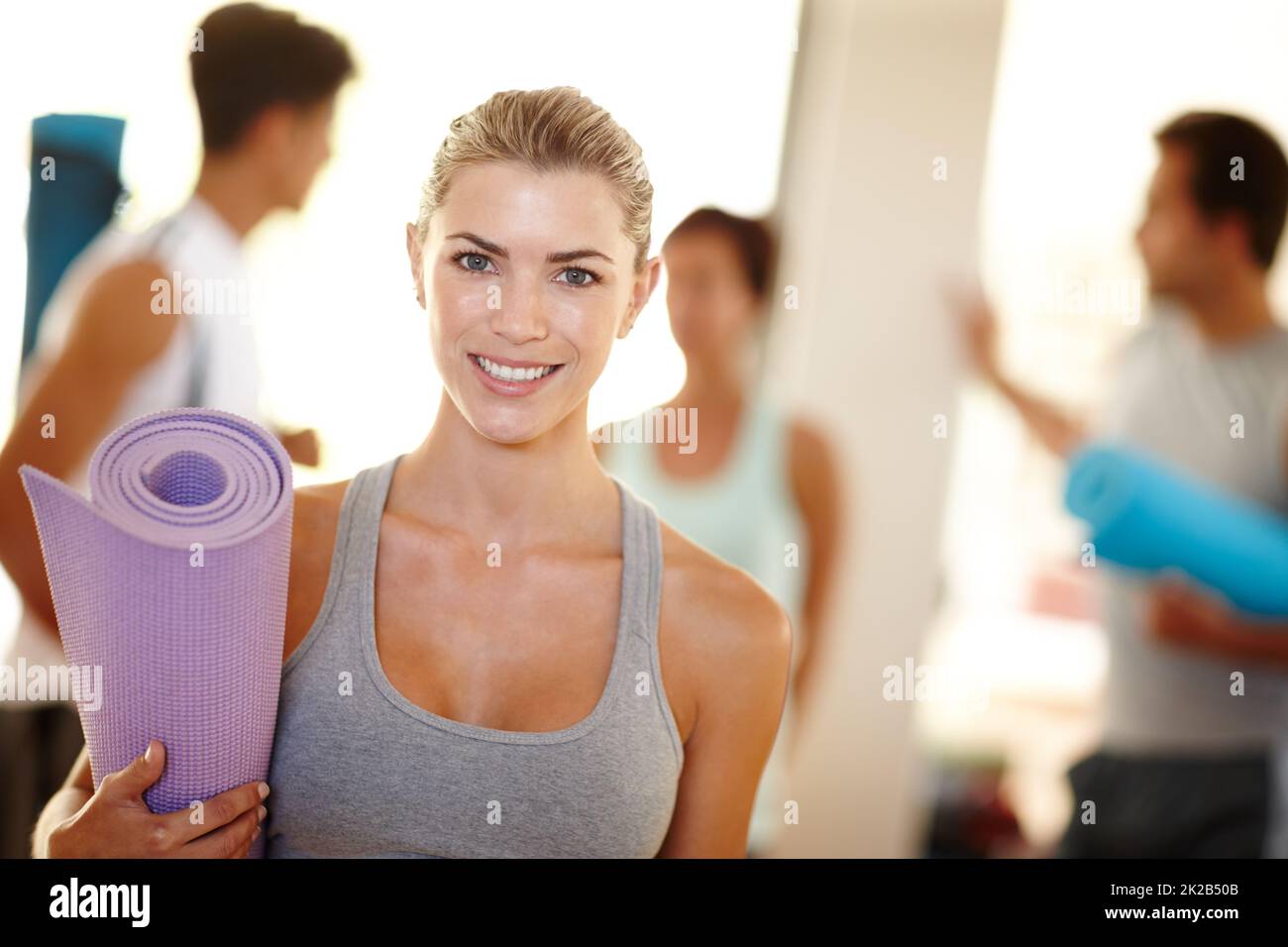 Ich liebe es, Teil dieser Yoga-Klasse zu sein. Porträt einer schönen Frau mit ihrer Yogamatte und Menschen im Hintergrund. Stockfoto
