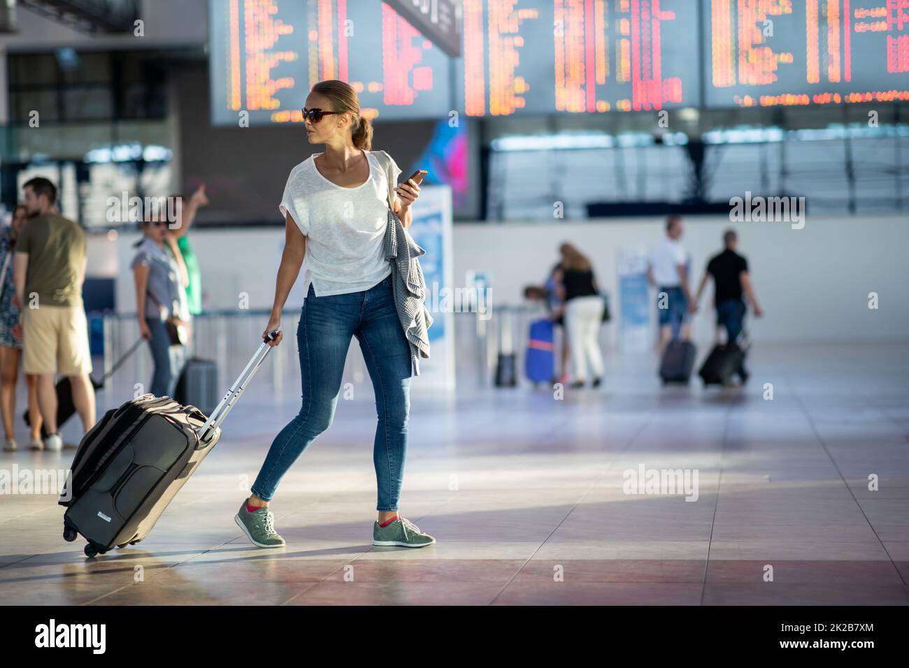 Junge Frau mit ihrem Gepäck an einem internationalen Flughafen, bevor es durch den Check-in die Sicherheit prüfen Sie vor Ihrem Flug und Stockfoto