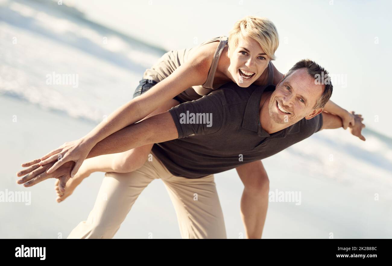 Für immer verspielt. Ein Mann gab seiner Frau eine Huckepack-Fahrt am Strand. Stockfoto