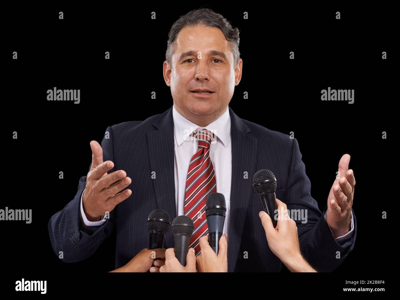Der Presse. Porträt eines reifen Mannes, der auf schwarzem Hintergrund eine Pressekonferenz gibt. Stockfoto