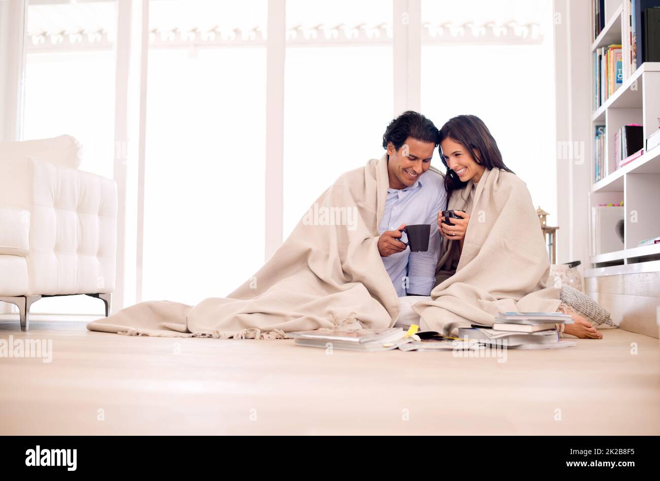 Das Beste aus ihrer Zeit zusammen zu machen. Aufnahme eines jungen Paares, das in eine Decke gehüllt auf dem Boden sitzt und Fotoalben ansieht. Stockfoto