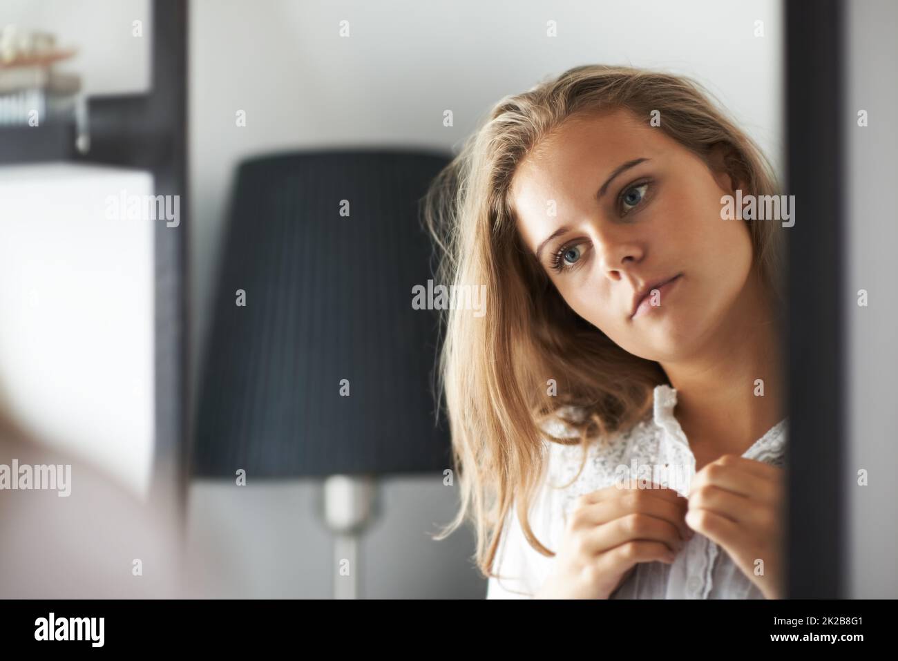 Ihre Reflexion einnehmend. Eine junge Frau, die sich anzieht, während sie in den Spiegel schaut. Stockfoto
