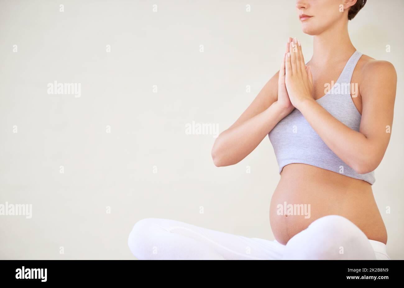Halten Sie ihren Körper und Geist in guter Form für das Baby. Eine junge, schwanger sitzende Frau in einer Yoga-Pose - abgeschnitten. Stockfoto