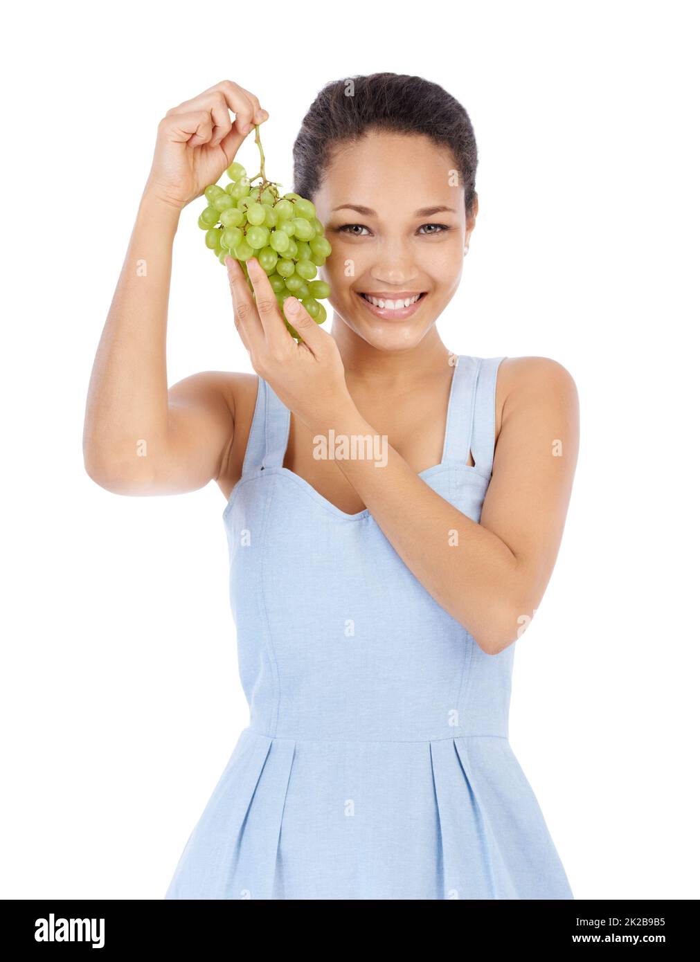 Frisch und saftig. Junge Frau lächelt, während sie ein Traubenbündel hochhält - isoliert auf Weiß. Stockfoto